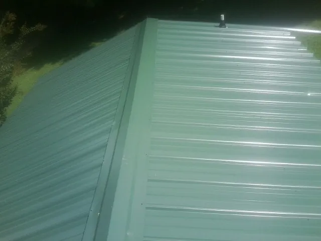 New green metal panels meeting at the ridge of a roof — Flat Roof Repair work by our crew in Valdosta