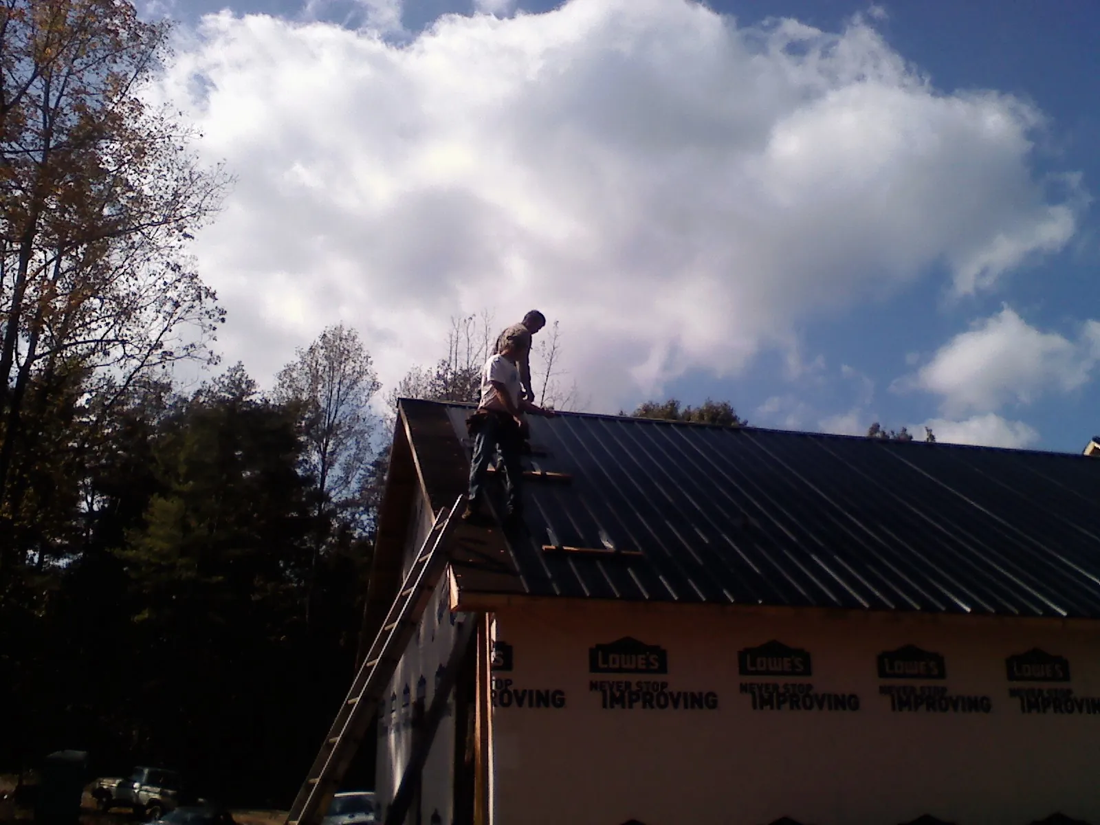 Roofer fastening dark metal panels high against a cloudy sky, from a Roof Inspection job in Valdosta