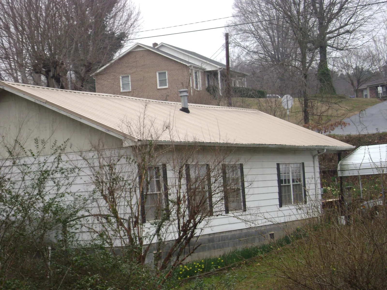 Tan metal roof on a white sided house set into a hillside — Commercial Roofing by Roofing Brothers in Valdosta
